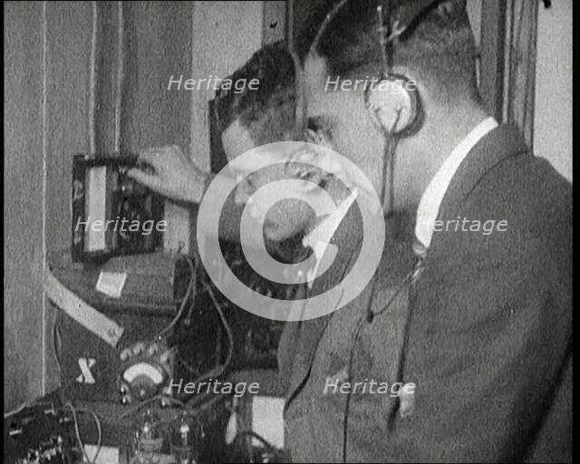Two Men Wearing Headphones and Calibrating Wireless Equipment, 1922. Creator: British Pathe Ltd.