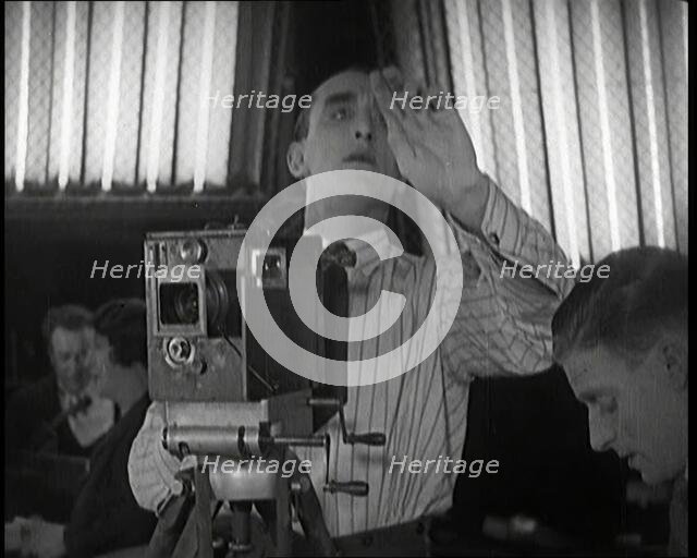 A Male Cameraman Films a Scene Whilst Lights Illuminate Behind Him, 1920s. Creator: British Pathe Ltd.