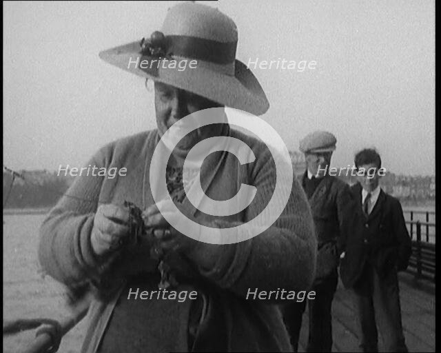 Female Civilian Removing Seaweed from a Fishing Hook Whilst Fishing from a Pier, 1920. Creator: British Pathe Ltd.