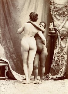 Two women posing naked in a photographic studio, standing embracing each other in front..., c1900. Creator: Unknown.
