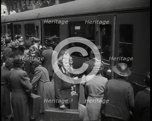Male and Female Passengers, Some Holding Suitcases, on a Platform of a Large Train Station..., 1938. Creator: British Pathe Ltd.