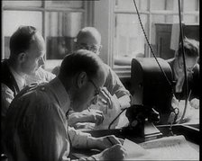 Four Male British Journalists Sitting Around a Table Covered in Papers and Writing, 1939. Creator: British Pathe Ltd.