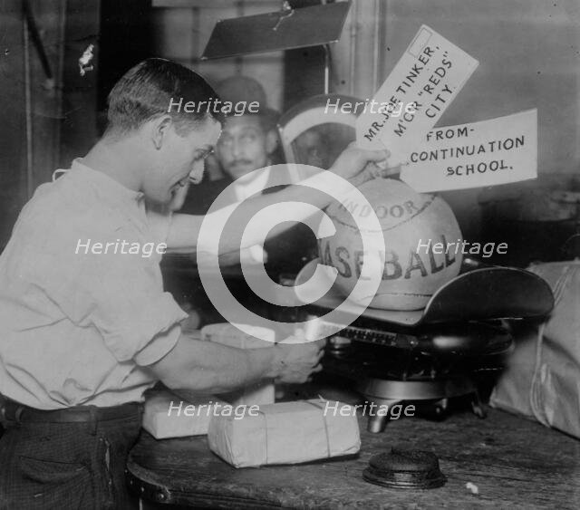 Medicine ball being weighed by Post Office employee; shipping tags read: Mr. Joe Tinker..., 1913. Creator: Bain News Service.