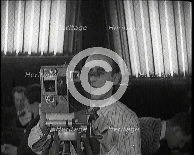 A Male Cameraman Films a Scene Whilst Lights Illuminate Behind Him, 1920s. Creator: British Pathe Ltd.
