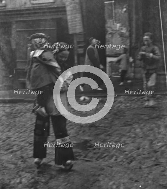 Woman carrying a child crossing a street, Chinatown, San Francisco, between 1896 and 1906. Creator: Arnold Genthe.