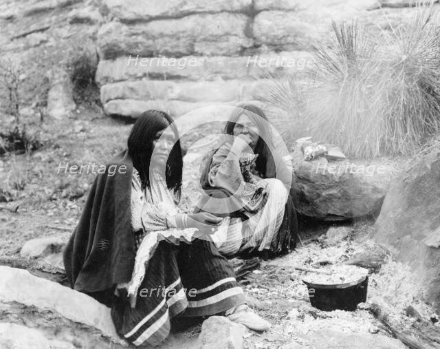 Two Apache Indian women at campfire, cooking pot in front of one, c1903. Creator: Edward Sheriff Curtis.