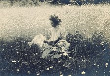 Woman with wreath of leaves in her hair sitting in a field of daisies, c1900. Creator: Unknown.