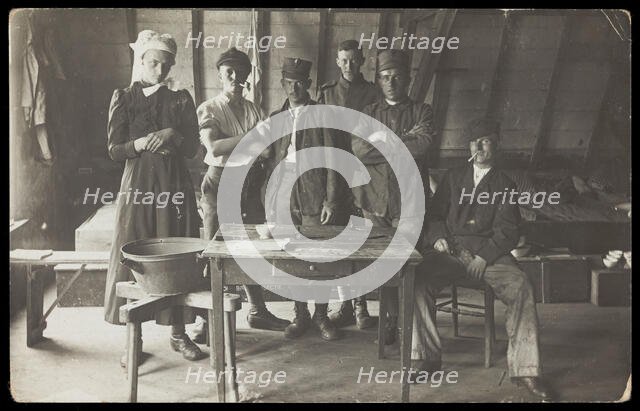 French prisoners of war, one in drag, gather round a small wooden table, [between 1910 and 1919?]. Creator: Unknown.