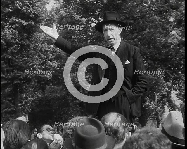 A Close up of a British Man in Dark Suit and Hat Declaiming Before a Crowd from a Raised..., 1938. Creator: British Pathe Ltd.
