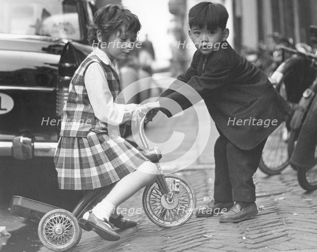 Children playing with a tricycle, c1960s.