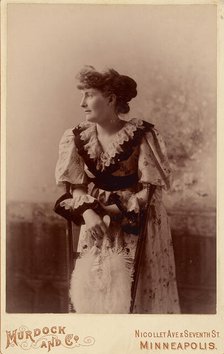 Unidentified woman in profile, leaning on a chair, holding a feather fan, about 1890. Creator: Murdock and Company.