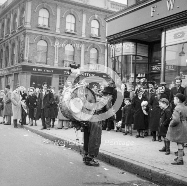 One-man band performing in front of a crowd outside Woolworths, Camden, London, 1952. Artist: Henry Grant