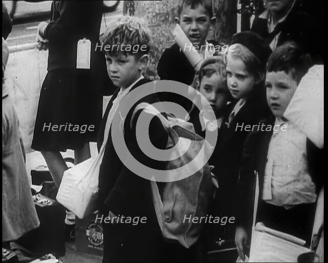 British Child Evacuees Standing on a Pavement With Bags and Boxes as Adults are Standing..., 1939. Creator: British Pathe Ltd.