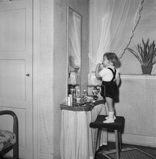 A little girl uses her mother's lipstick in front of a mirror, Sweden. Artist: Unknown