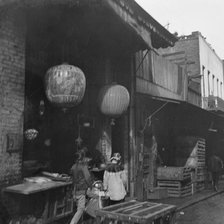 Two women and a child walking down a sidewalk betwen crates, Chinatown, San Francisco, c1896-1906. Creator: Arnold Genthe.