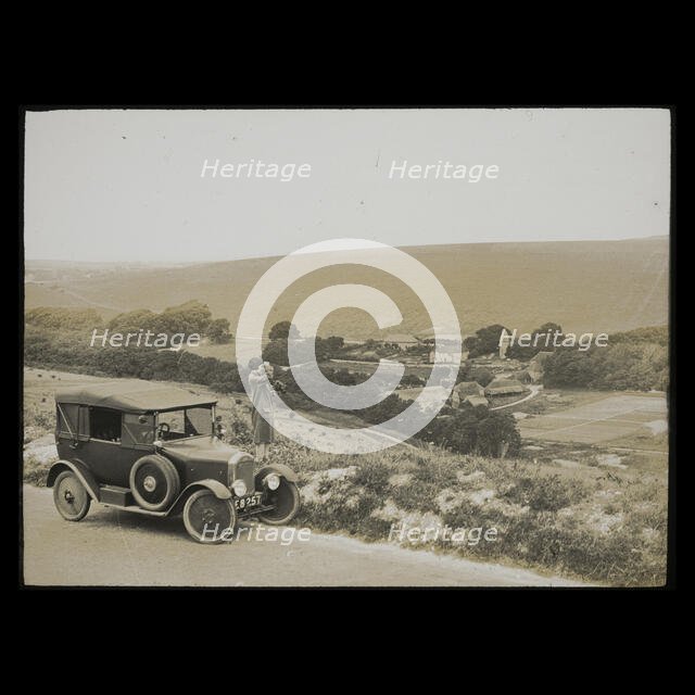 A woman standing beside a car parked on East Dean Road near Exceat Hill, looking out..., 1921-1939. Creator: Norman Kingsley Harrison.