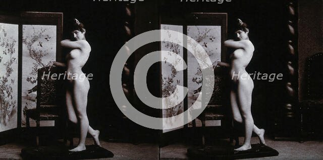 A young woman posing naked in a photographic studio, leaning on the back of a chair..., c1900. Creator: Unknown.