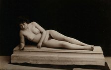 A young woman posing naked in a photographic studio, lying on a wooden plinth, approx 1900. Creator: Unknown.