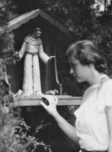 Brady, Victoria, Miss, with a statue of St. Francis in a garden, 1931 July 14. Creator: Arnold Genthe.