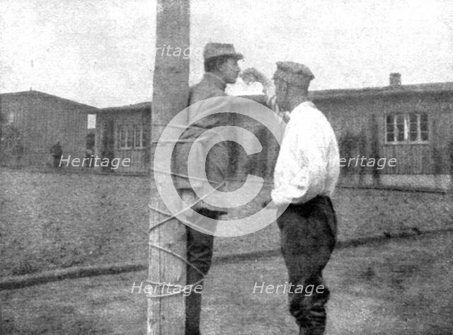 'La peine du poteau; a Zwickau: un Francais, lie au poteau, recoit d'un prisonnier roumain..., 1917. Creator: Unknown.