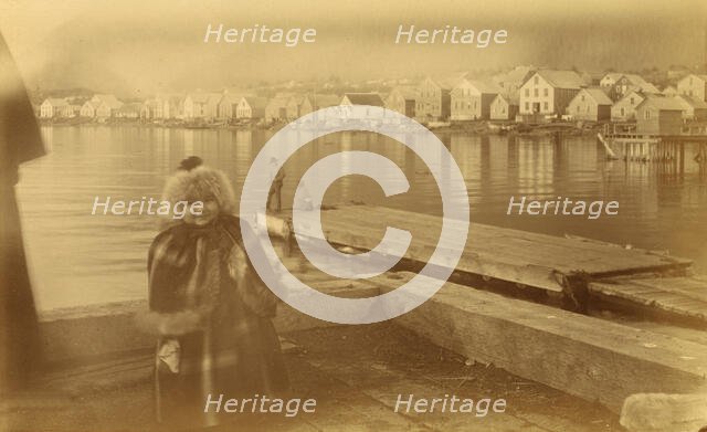 Unidentified young girl standing on wharf, with buildings along waterfront...,1894 or 1895. Creator: Alfred Lee Broadbent.