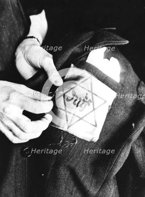 Sewing the yellow star identifying a Jew onto a jacket, German-occupied Paris, 1942. Artist: Unknown