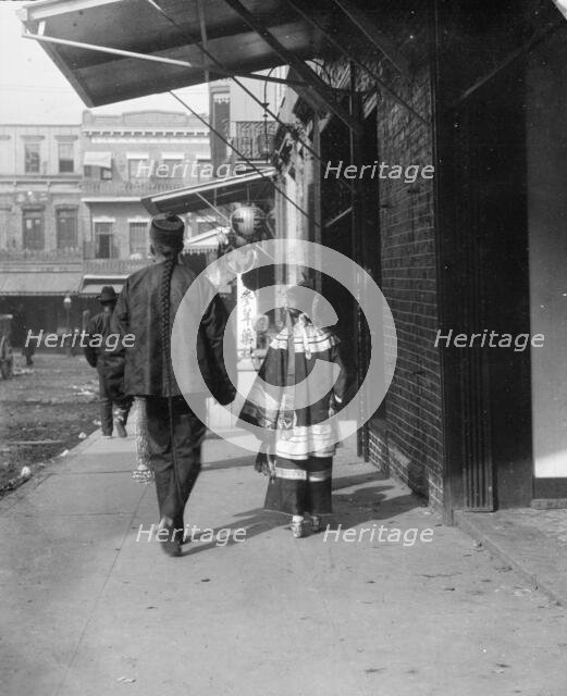 Man and a young girl walking down a sidewalk, Chinatown, San Francisco, between 1896 and 1906. Creator: Arnold Genthe.