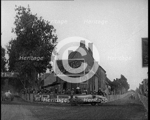 A Racing Circuit As Racing Cars Drive By. Signs On a Building Read: 'Spidoleine Huile' and..., 1924. Creator: British Pathe Ltd.