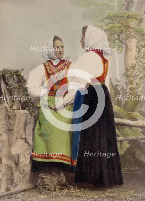 Two young women pose in folk costumes, with dotted headdresses, 1886-1890. Creator: Helene Edlund.
