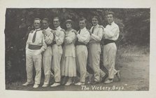 Entertainers, one in drag, pose in a line in front of foliage, [between 1910 and 1919?]. Creator: Unknown.