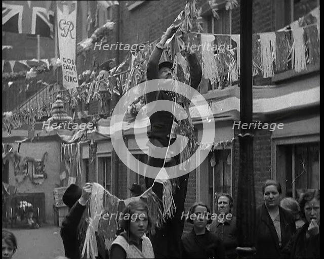 Man Hanging Bunting from a Lamp Post in a Street With Decorations For the Coronation of..., 1937. Creator: British Pathe Ltd.