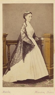 Unidentified woman wearing a white dress and black shawl, standing, 1870-1875. Creator: H. R. Marks.