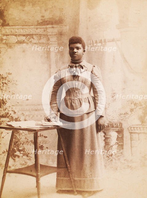 Studio portrait of woman, hand on books spread on table, (1880-1940?). Creator: Madison Art Studio.