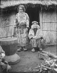 Ainu man and seated woman at the entrance of a hut, 1908. Creator: Arnold Genthe.