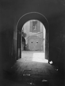 View of a courtyard through an arched passageway, New Orleans, between 1920 and 1926. Creator: Arnold Genthe.