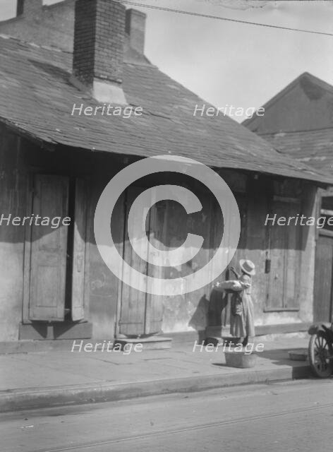 Woman holding a sack standing by the doorway of a building in the French Quarter..., c1920-c1926. Creator: Arnold Genthe.