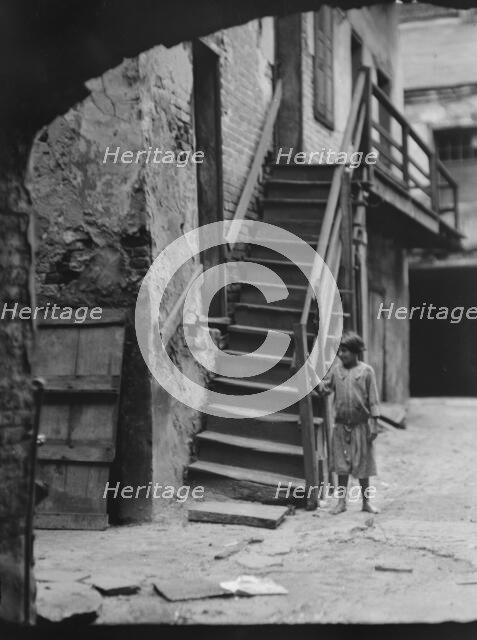 Child standing next to a stairway in a courtyard, New Orleans, between 1920 and 1926. Creator: Arnold Genthe.