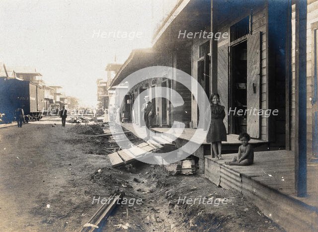 Colón, Panama: unpaved street lined with wooden houses; two children watch from a porch..., 1906. Creator: Unknown.
