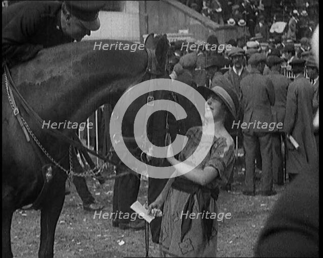A Female Civilian Wearing a Dress and a Large Hat with a Ribbon Petting a Horse on the Nose at a Hor Creator: British Pathe Ltd.