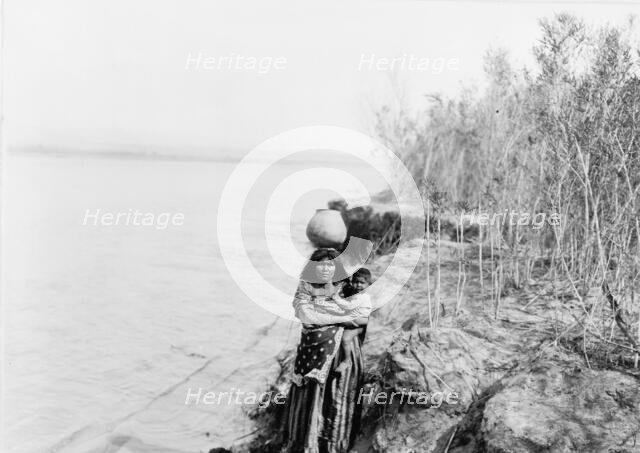 Mohave woman carrying water on her head and holding child, c1903. Creator: Edward Sheriff Curtis.
