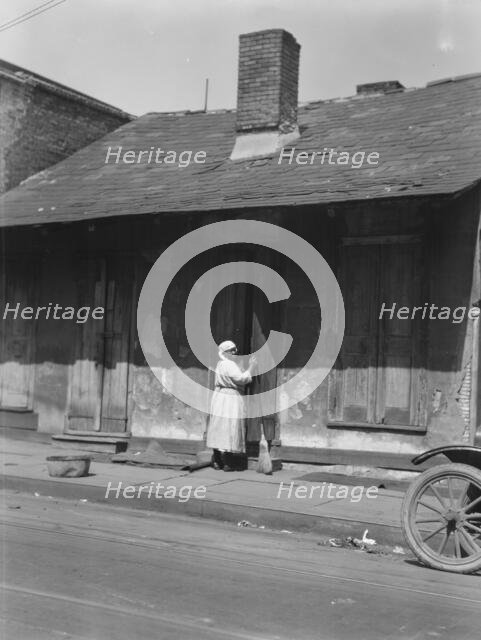 View from across street of a woman with a broom standing in a doorway, New Orleans, c1920-c1926. Creator: Arnold Genthe.