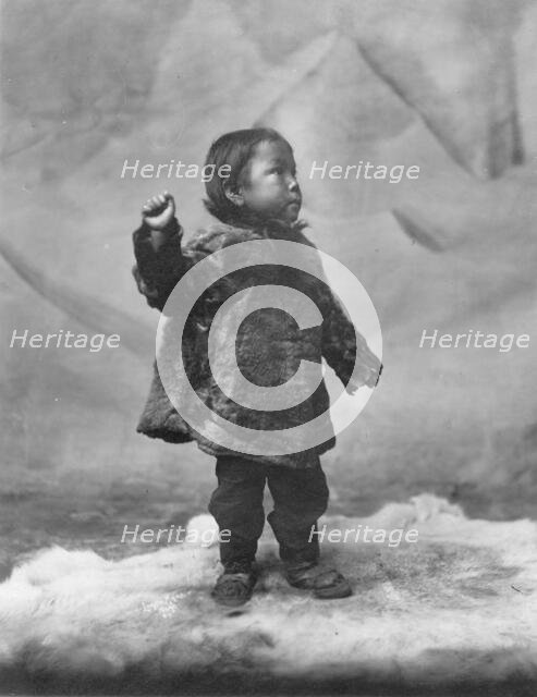 Eskimo child posing while standing on fur rug, between c1900 and c1930. Creator: Unknown.