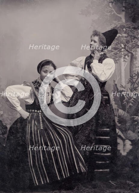 Studio portrait of two young girls posing in folk costumes from Dalarna, 1880-1907. Creator: Helene Edlund.