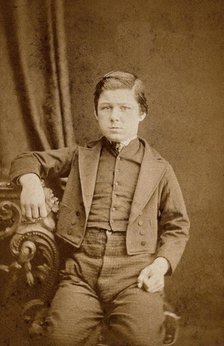 A seated young man with clenched fists, leaning against an ornate table, c1890s. Creator: AE Scales.