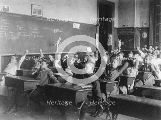 Children seated at desks in Washington, D.C. classroom, stretching, (1899?). Creator: Frances Benjamin Johnston.