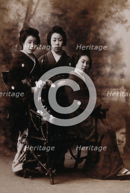 Three young women posing in a photographic studio, one seated on a bench..., early 20th century. Creator: Unknown.