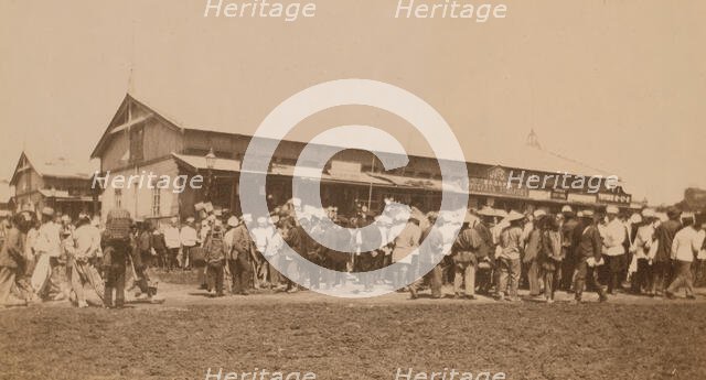 Crowds of people in front of buildings at the marketplace in the center of town..., (1899?). Creator: Eleanor Lord Pray.