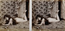 A young woman posing naked in a photographic studio, lying on her front on a piece of..., c1900. Creator: Unknown.