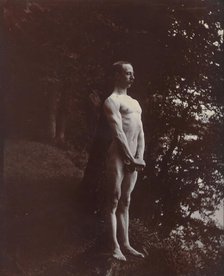 A man posing naked, standing with his chest out, arms down and hands clasped, approx 1900. Creator: Unknown.