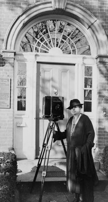 Frances Benjamin Johnston, full-length portrait, standing in front of door, with camera..., c1935. Creator: Unknown.